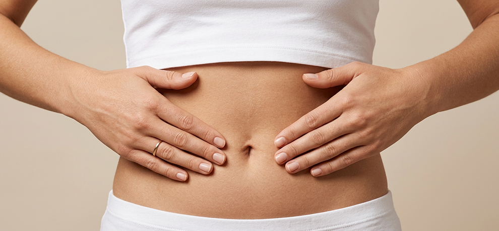 Gros plan sur les mains d'une femme posees sur son ventre en geste d'auto-massage pour soulager la digestion sur fond beige neutre
