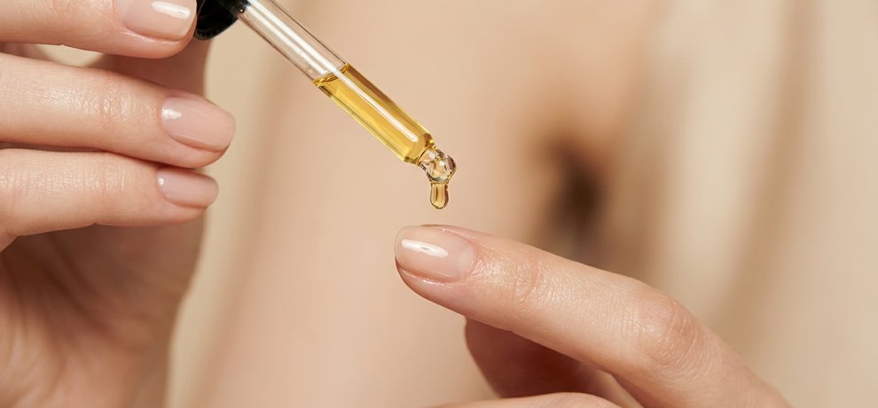 Gros plan sur des mains aux ongles naturels et sains avec une pipette en verre sur fond neutre clair en lumière douce
