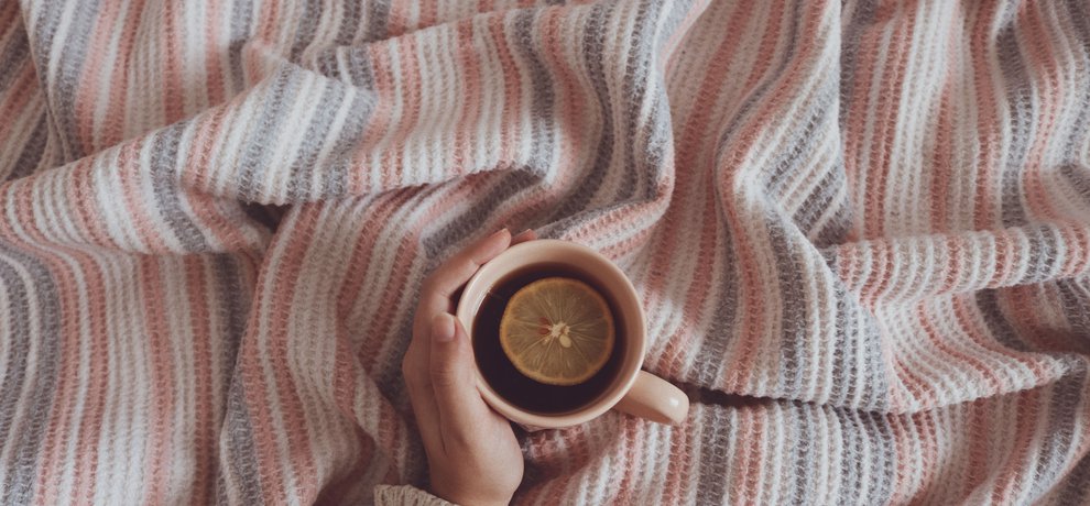 Main tenant une tasse de tisane chaude au citron posée sur un plaid en laine